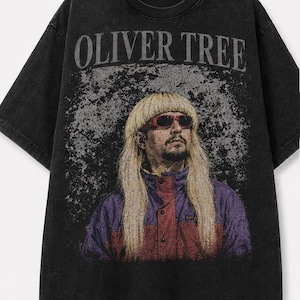 May include: A black short-sleeve t-shirt with a distressed graphic print featuring the text OLIVER TREE in an arched font above a portrait of a person with a blonde bowl cut, red sunglasses, and a purple and red jacket against a textured background.