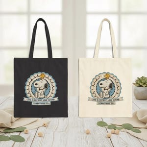 May include: Two tote bags, one black and one cream-colored, each featuring a circular design with Snoopy and Woodstock. The design includes the text "LOVE IS PATIENT, LOVE IS KIND. 1 CORINTHIANS 13:4" on a banner.