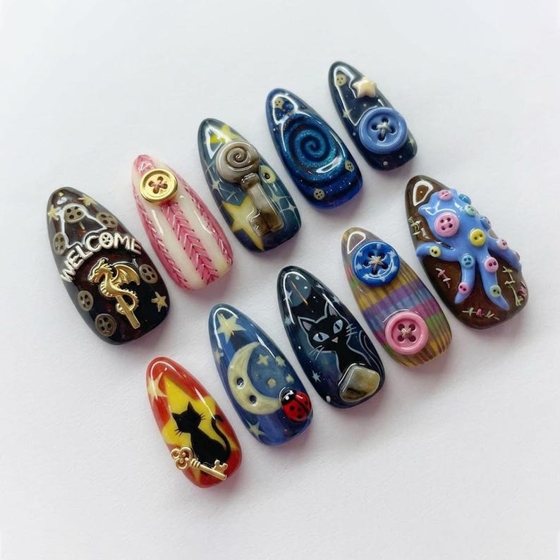Puede incluir: Una colecci&oacute;n de diez u&ntilde;as postizas con forma de almendra y dise&ntilde;os &uacute;nicos. Cada u&ntilde;a presenta dise&ntilde;os intrincados pintados a mano, incluyendo un gato, una llave, una luna, estrellas, botones y un pulpo. Los colores incluyen negro, azul, rojo, amarillo y rosa.