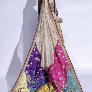 May include: An ornate, embroidered garment with a long, flowing train. The train features vibrant panels of purple, pink, yellow, and teal, adorned with intricate floral and bird motifs. The garment's main body is a cream color with gold embroidery, and the edges are trimmed with a deep red.