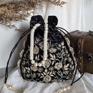 May include: Black velvet drawstring bag with gold floral embroidery and pearl detailing. The bag has a beaded pearl handle and pearl tassel drawstrings. A decorative accessory.