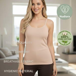 Puede incluir: Camisola beige con tirantes finos. La imagen incluye el texto "Trusted Quality", "24/7 Comfort", "Breathable Fabric" y "Hygienic Material". Un logotipo circular indica "100% Pure Cotton For Your Comfort". También es visible la marca "Nudiora".