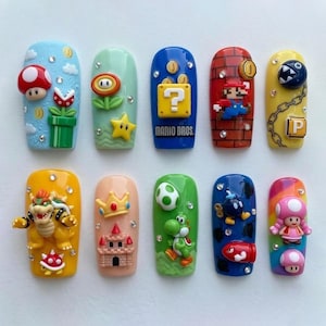 May include: A set of ten long, oval-shaped acrylic nails, each decorated with a different Super Mario Bros. character or element. Designs include Mario, Bowser, Yoshi, and various power-ups, set against colorful backgrounds with rhinestone accents.