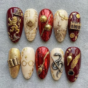 Könnte beinhalten: Zehn mandelförmige Nageldesigns mit Harry-Potter-Motiven. Jeder Nagel zeigt aufwendige 3D-Verzierungen und Designs, darunter ein Löwe, eine Karte, ein Schnatz, ein Schloss, eine Truhe, ein Buch, eine Brille, ein Besen, eine Schlange und eine Feder.