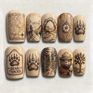 May include: A collection of ten wooden decorative pieces, each with a unique outdoor-themed design. The designs include a map, mountain scene, archway, compass, bear paw prints, and Smokey Bear. The text "Trail Map - Peak Explorers" and "Bear Tracks" are visible.