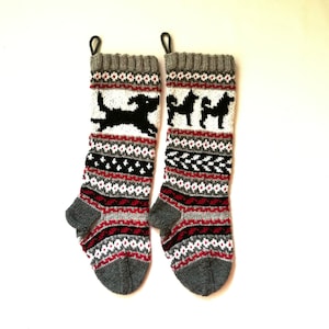 May include: Pair of gray, red, white, and black knitted Christmas stockings with a dog silhouette design.