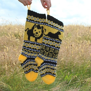 May include: Two knitted Christmas stockings with a yellow, black, and white pattern. The stockings feature a lion design and are hanging from a hand.
