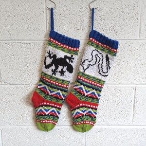 May include: Two knitted Christmas stockings with a blue, red, green and white pattern. One stocking features a black gecko, and the other features a white snake.