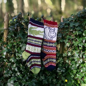 May include: Two knitted Christmas stockings with green, red, white and blue stripes. One stocking features a white alligator and the other features a white hippopotamus.