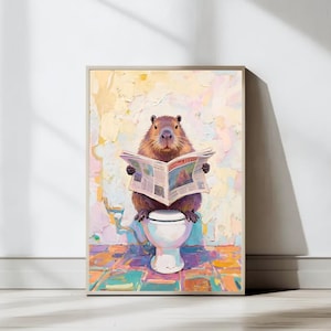 May include: A framed art print depicts a capybara sitting on a toilet, engrossed in reading a newspaper. The artwork features a colorful, textured background with a whimsical, humorous theme. The capybara is brown, and the toilet is white.