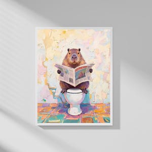 May include: A framed art print depicts a capybara sitting on a toilet, engrossed in reading a newspaper. The artwork features a colorful, textured background and a tiled floor. The capybara is brown with a focused expression.