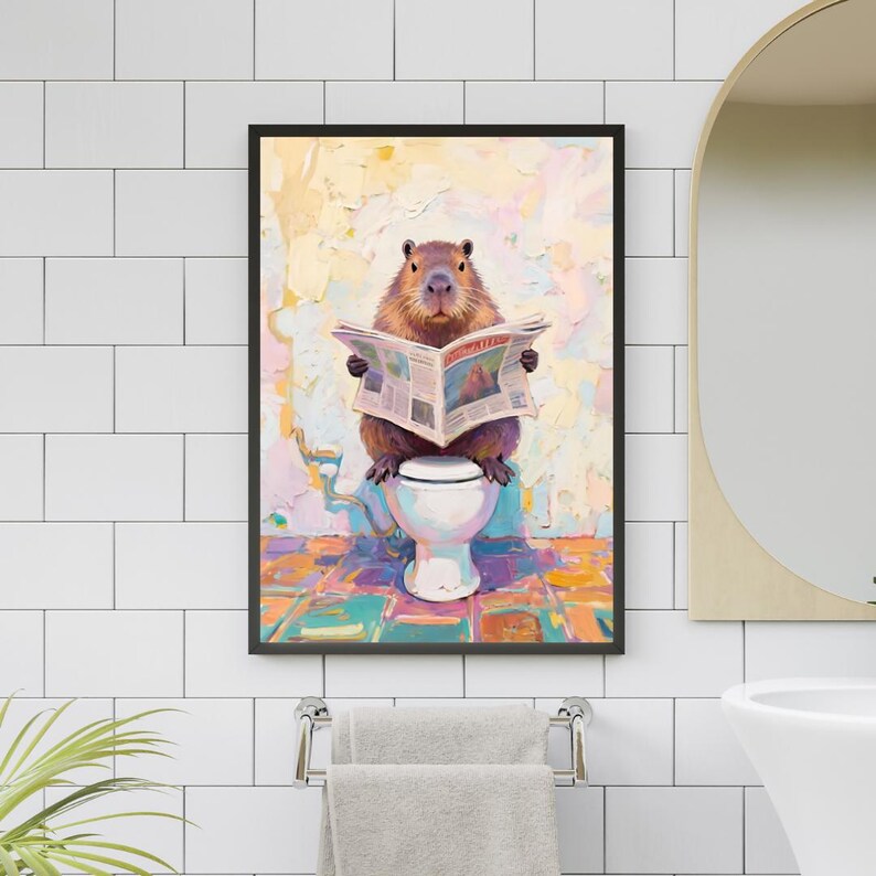 May include: A framed art print depicts a capybara sitting on a toilet, engrossed in reading a newspaper. The artwork features a colorful, textured background with a whimsical, humorous theme. The capybara is brown, and the toilet is white.