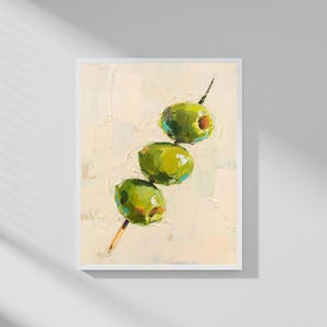 May include: An oil painting of three green olives on a skewer. The olives are painted with visible brushstrokes, and the background is a textured off-white. The artwork is framed in a white border.
