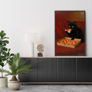 May include: A framed print featuring a black cat enjoying pizza. The cat, with yellow eyes, is seated on a red couch, holding a slice of pizza. A pizza box with two slices is in front of the cat. The artwork is displayed above a black cabinet.