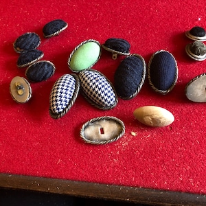 May include: Assortment of oval-shaped buttons in various colours and patterns, including black, green, white, and blue. Some buttons have a rope-like trim around the edges.