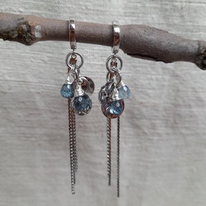 May include: A pair of silver hoop earrings with dangling chains and blue gemstone accents.
