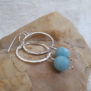 Może przedstawiać: Srebrne kolczyki koła z fakturą młotkową i niebieskim kamieniem wiszącym.