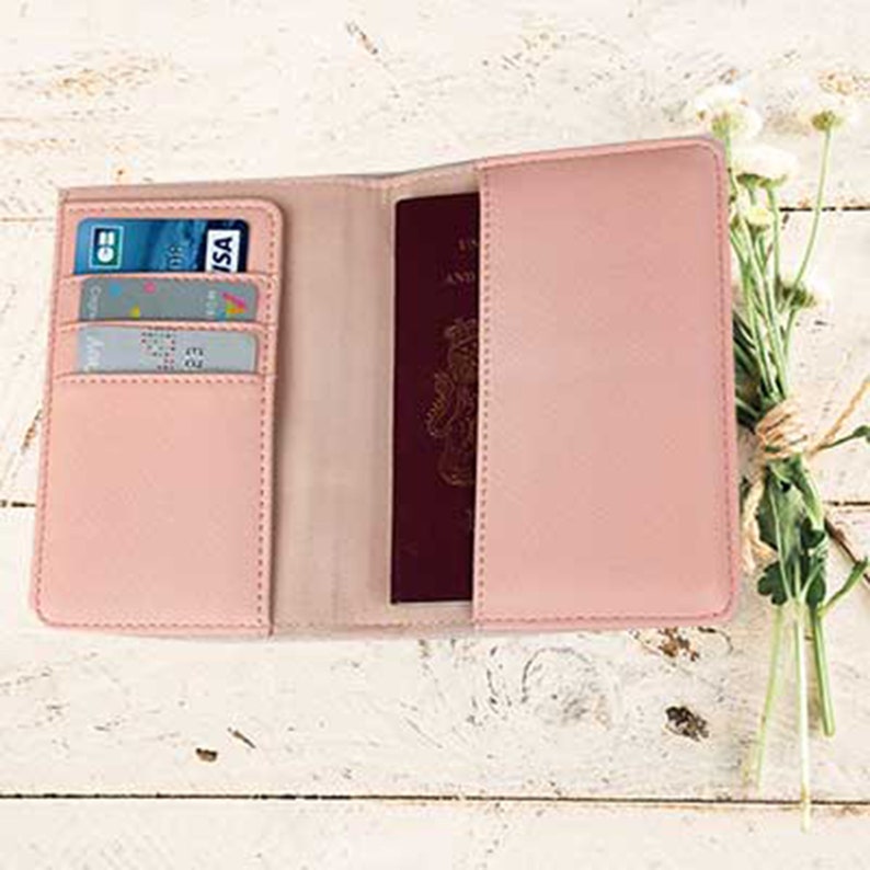 May include: A pink passport holder with a slot for cards and a separate compartment for a passport. The holder is open and shows a passport and credit cards inside.