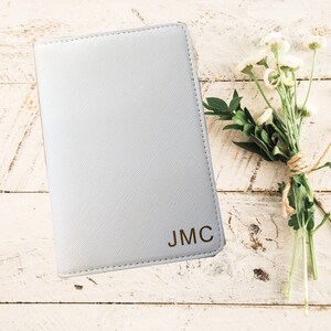 May include: A white passport holder with the initials JMC embossed in gold on the front.