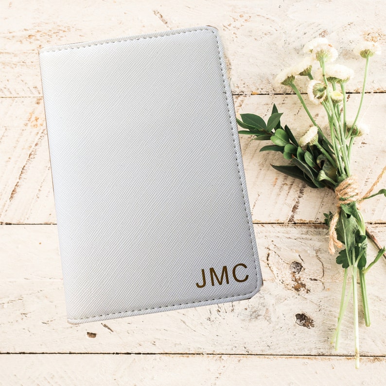 May include: A white passport holder with the initials JMC embossed in gold on the front.