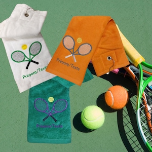 Peut inclure: Trois serviettes de bain blanches, orange et vertes avec des raquettes de tennis et une balle de tennis brodées. Les serviettes ont une boucle pour accrocher et le texte "Prénom/Texte" est brodé sur chaque serviette.