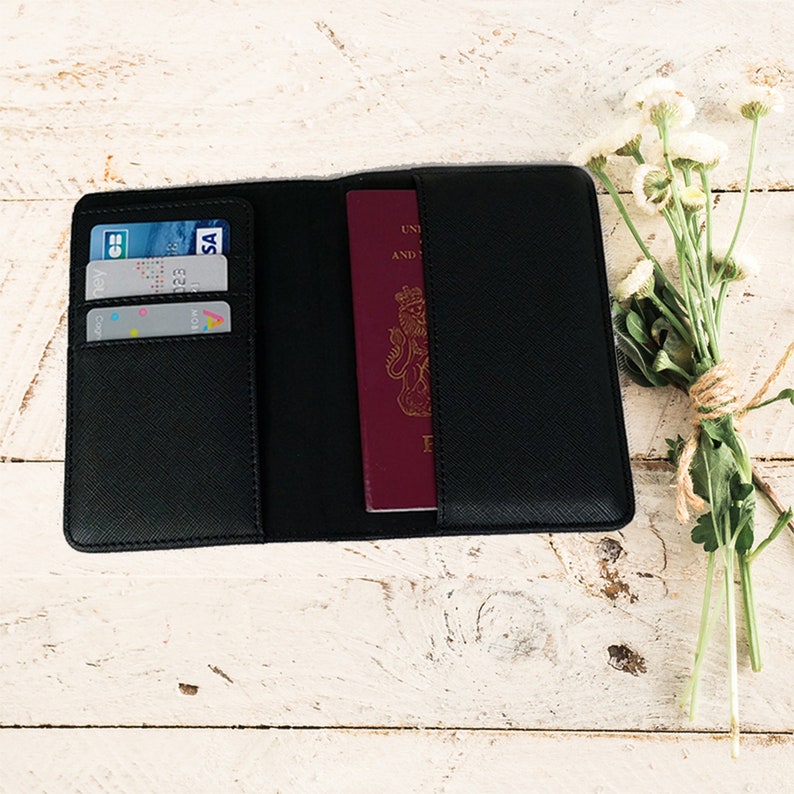 May include: A black passport holder with a burgundy passport inside. The holder has a slot for cards and is open to reveal the passport.