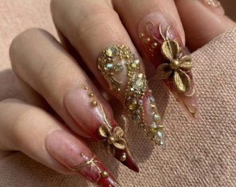 Uñas postizas con diseño de flor dorada y stilettos, con juego de diamantes de imitación en color burdeos degradado