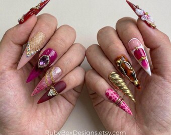 Uñas postizas de aguja en rojo intenso: cadenas doradas, piedras de estrás y metal esculpido.