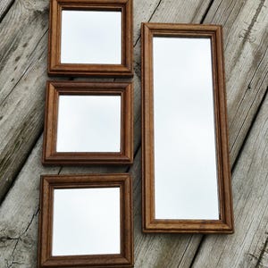 May include: A set of four wall mirrors with medium-toned brown wooden frames. The collection includes three square mirrors of identical size and one rectangular mirror that is significantly taller, all featuring a simple, classic molding design.