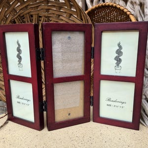 May include: A tri-fold burgundy wooden picture frame. Each panel has a rectangular opening with a cream-colored backing. The top and bottom panels display a black and white drawing of a topiary. The text "Renderings" and "SIZE: 2 1/2" x 3"" are visible.