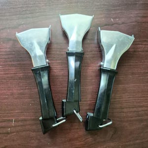 May include: Three detachable cookware handles with a metallic silver finish on the upper portion and a solid black plastic grip on the lower portion. Each handle features a small metal loop at the base for hanging and a mechanism for attachment.