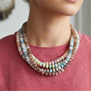 May include: A multi-strand necklace featuring a variety of pastel-colored beads. The necklace includes shades of pink, blue, green, and brown. The beads are strung together, creating a layered effect. The necklace is worn around the neck.