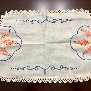 以下が含まれることがあります： ピンク、ブルー、グリーンの刺繍が施された、白の麻製のテーブルランナー。クロシェの縁取りと、渦巻きとドットの繰り返し模様が特徴です。