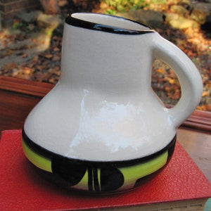 Pode incluir: Caneca de cerâmica branca com borda preta e design geométrico em preto, verde e amarelo.