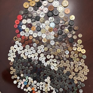 Könnte beinhalten: Eine große Sammlung verschiedener Nähknöpfe in unterschiedlichen Größen, Formen und Farben, darunter Weiß, Schwarz, Braun, Beige, Rot und Blau. Die Knöpfe weisen verschiedene Lochzahlen, Texturen und Oberflächen auf und sind dicht angeordnet.