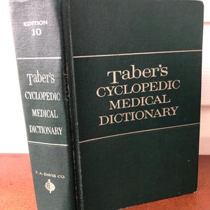 Puede incluir: Un libro de tapa dura verde titulado "Taber's Cyclopedic Medical Dictionary" con el número de edición 10 en el lomo. El libro está publicado por F.A. Davis Co.