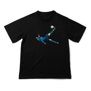 May include: Black t-shirt featuring a soccer player in a blue uniform kicking a soccer ball. The player is mid-air, executing a bicycle kick. The soccer ball is white with black pentagons.