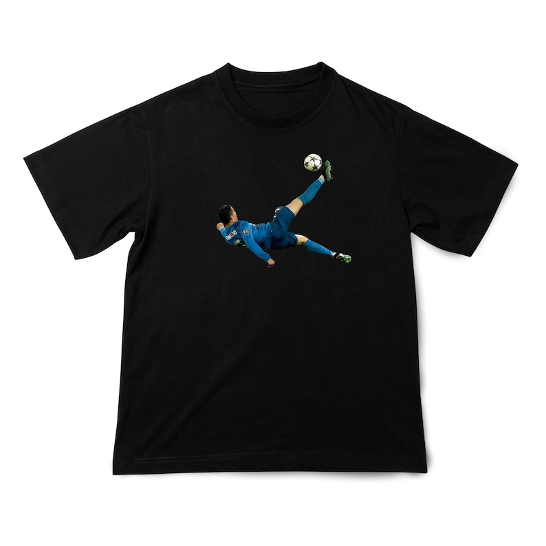 May include: Black t-shirt featuring a soccer player in a blue uniform kicking a soccer ball. The player is mid-air, executing a bicycle kick. The soccer ball is white with black pentagons.