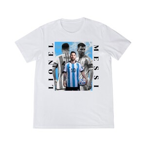 Puede incluir: Camiseta blanca con un gr&aacute;fico de Lionel Messi con la camiseta de Argentina. El dise&ntilde;o incluye im&aacute;genes de Messi en diferentes poses, con los nombres "MESSI" y "LIONEL" impresos verticalmente en los lados.