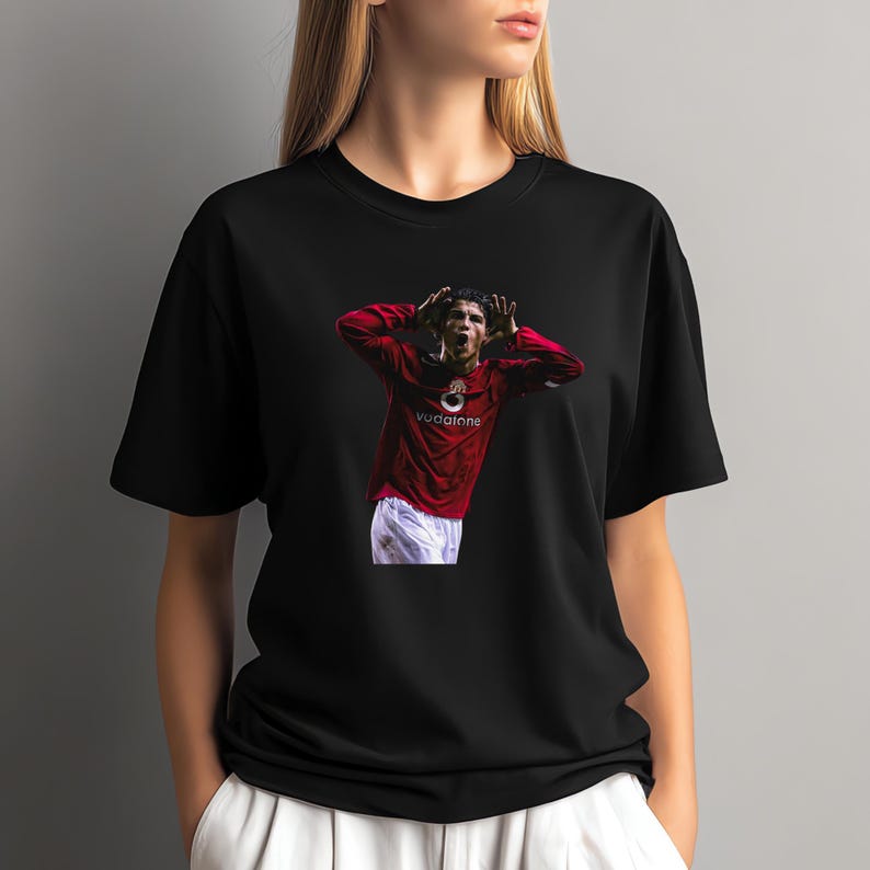 May include: Black t-shirt featuring a graphic of a soccer player in a red jersey with the Vodafone logo. The player is celebrating with his arms raised. The shirt is a crew neck.