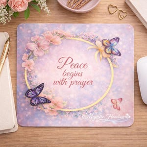 May include: A decorative mousepad with a floral and butterfly design. The mousepad features the text "Peace begins with prayer" in a script font, surrounded by a floral wreath. A white mouse is on the right.