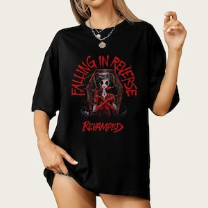 以下が含まれることがあります： 黒いTシャツ。赤いグラフィックは棺の中の女性で、「FALLING IN REVERSE」の文字が上にアーチ状に、下に「REVAMPED」の文字が描かれています。デザインはTシャツの前面にプリントされています。