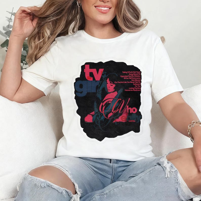 K&ouml;nnte beinhalten: Wei&szlig;es T-Shirt mit einem grafischen Design. Das Design zeigt den Text "TV Girl" in Blau und Rot und die Worte "Who Cares" in einer stilisierten Schriftart. Das Design enth&auml;lt eine Illustration einer Frau und Songtitel.