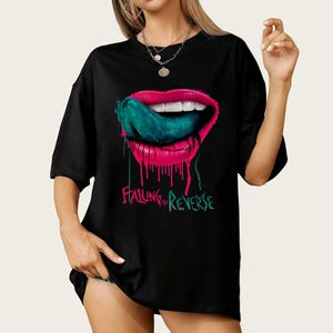 May include: Black t-shirt featuring a graphic of pink lips with a teal tongue sticking out. The lips have dripping pink paint. The text "Falling in Reverse" is in green below the lips.