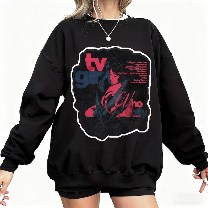 K&ouml;nnte beinhalten: Schwarzes Sweatshirt mit wei&szlig;em Kragen und Grafikdesign. Das Design zeigt die Worte "TV Girl" in Rot und Blau sowie eine Illustration einer Frau. Zus&auml;tzlicher Text ist sichtbar.