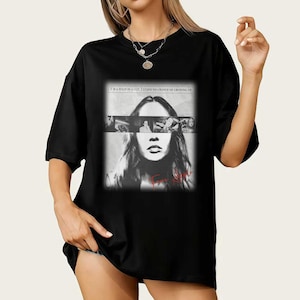 Może przedstawiać: Czarny t-shirt z czarno-białą grafiką przedstawiającą twarz kobiety i kolaż zdjęć. Nad obrazem wydrukowano tekst "I'M A TULIP IN A CUP. I STAND NO CHANCE OF GROWING UP."