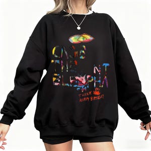 May include: Black sweatshirt with the text "CAGE THE ELEPHANT" in colorful, stylized letters. A colorful graphic of a shape is above the text. The words "THANK YOU HAPPY BIRTHDAY" are below the text.
