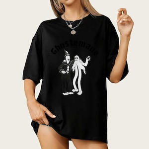 May include: Black t-shirt featuring a cartoon graphic of two figures, one dressed as a clown and the other as a ghost. The word "Ghostemane" is arched across the top in a stylized font. The shirt is a casual, oversized fit.