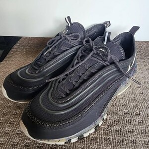 Puede incluir: Un par de zapatillas deportivas negras con un dise&ntilde;o texturizado. Las zapatillas tienen una suela blanca con detalles moteados y cordones negros. Las partes superiores presentan un dise&ntilde;o en capas con una mezcla de materiales y una burbuja de aire visible.