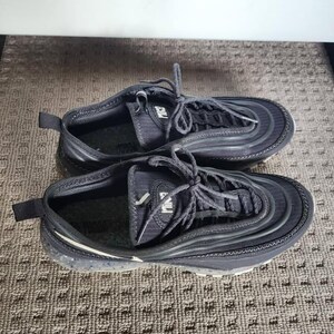 Puede incluir: Par de zapatillas deportivas negras con cordones. Las zapatillas tienen un dise&ntilde;o texturizado y una suela blanca con un patr&oacute;n moteado. Las zapatillas est&aacute;n sobre una superficie estampada.